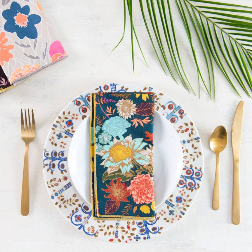 Colorful floral table setting with plates, napkins, and cutlery on a white surface.