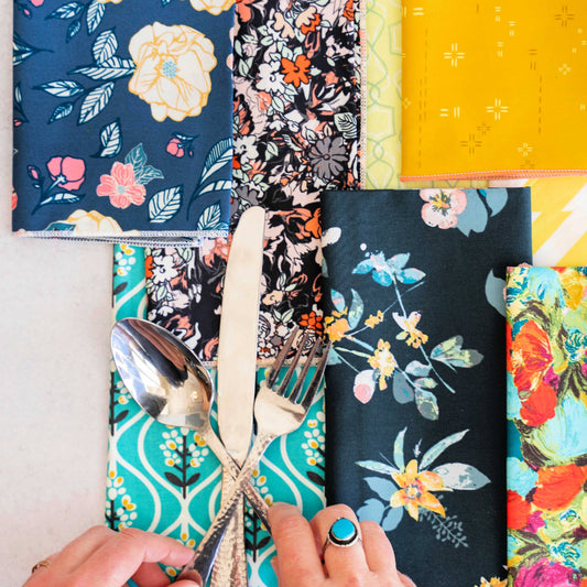 Colorful floral-patterned cutlery covers with a hand holding a spoon and fork.